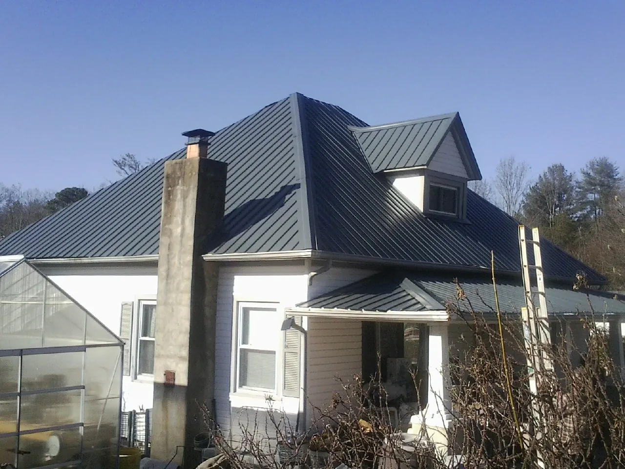 Dark blue standing seam metal roof on a white farmhouse with dormer — Slate & Tile Roof Repair by Roofing Brothers in Forest Lake