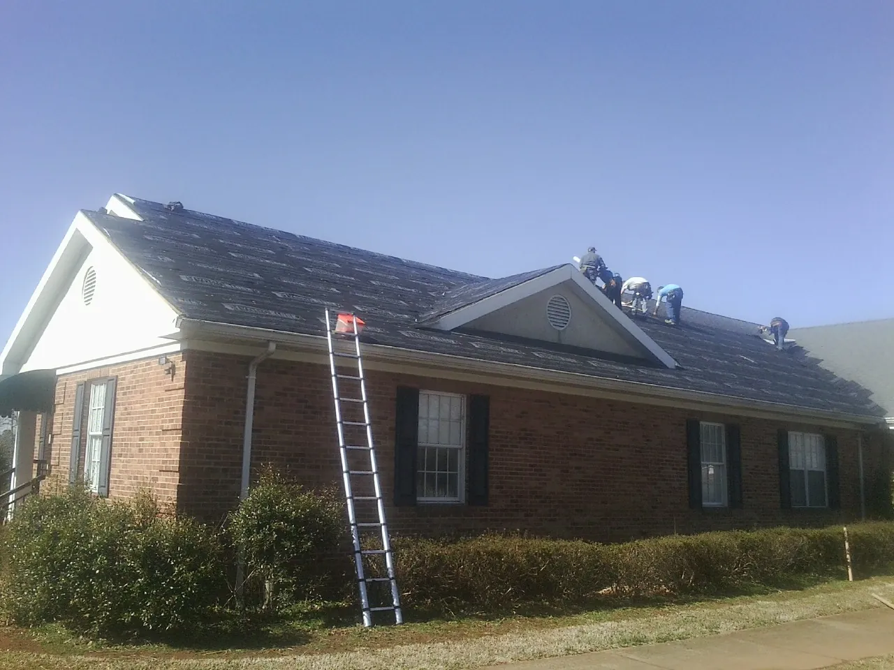 Crew tearing shingles off a brick ranch roof with a ladder set — Emergency Roof Repair work by our crew in Forest Lake