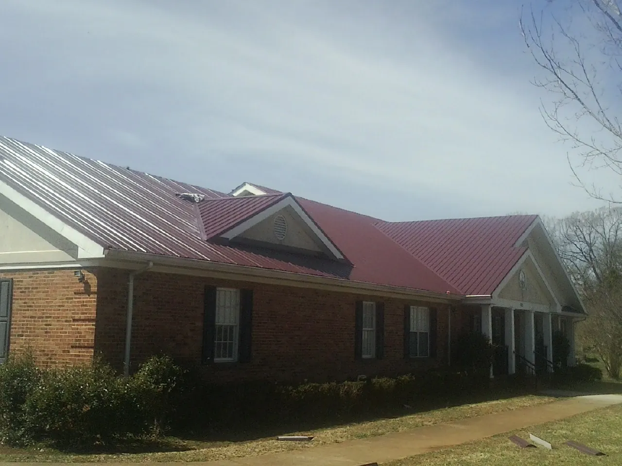 Red metal roof with gabled entries on a long brick building, from a Hail Damage Roof Repair job in Forest Lake
