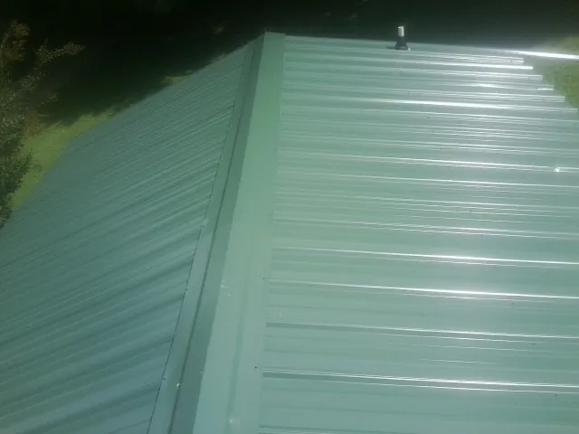 New green metal panels meeting at the ridge of a roof — Flat Roof Repair work by our crew in Forest Lake