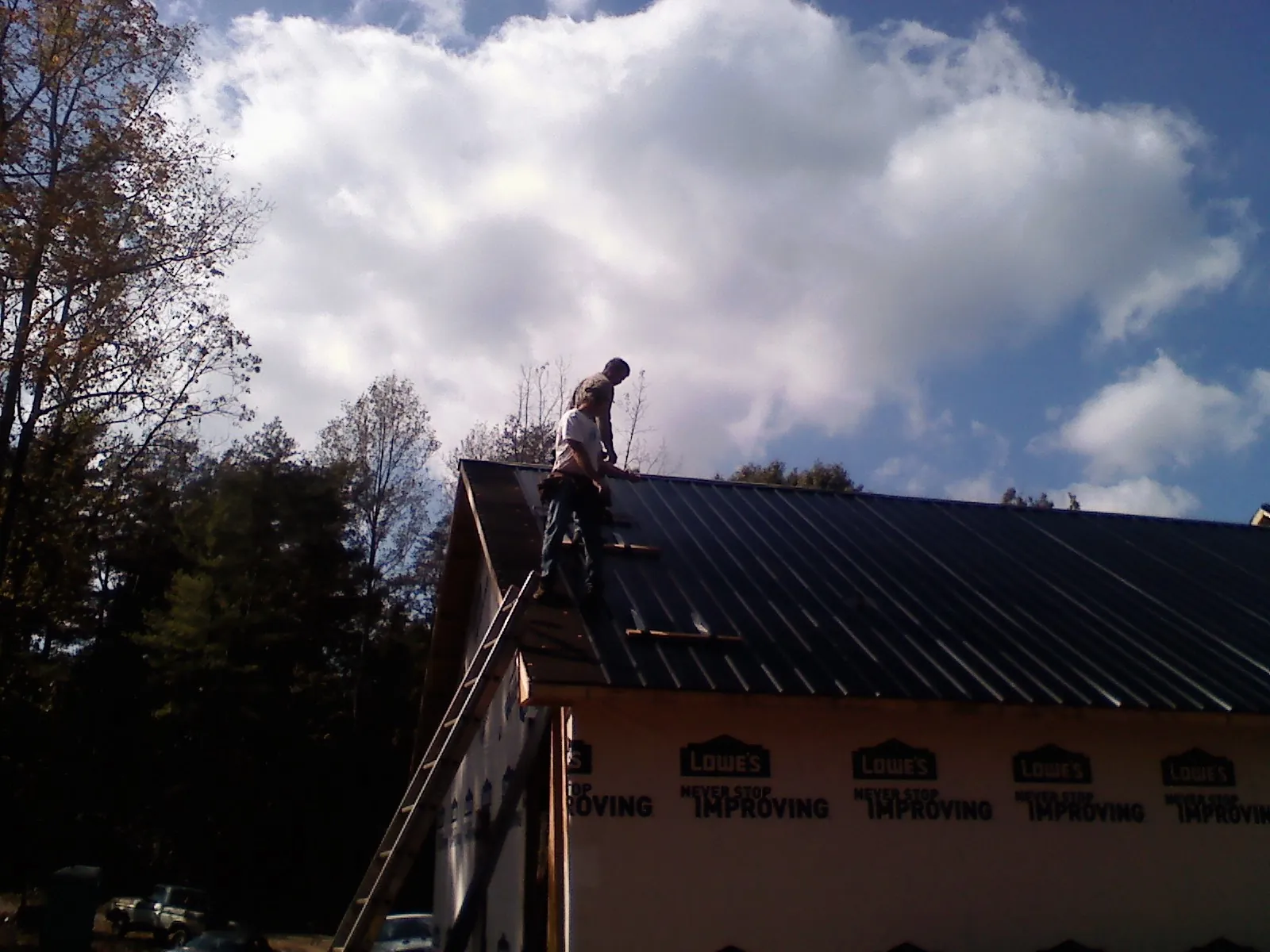 Roofer fastening dark metal panels high against a cloudy sky, from a Roof Inspection job in Forest Lake