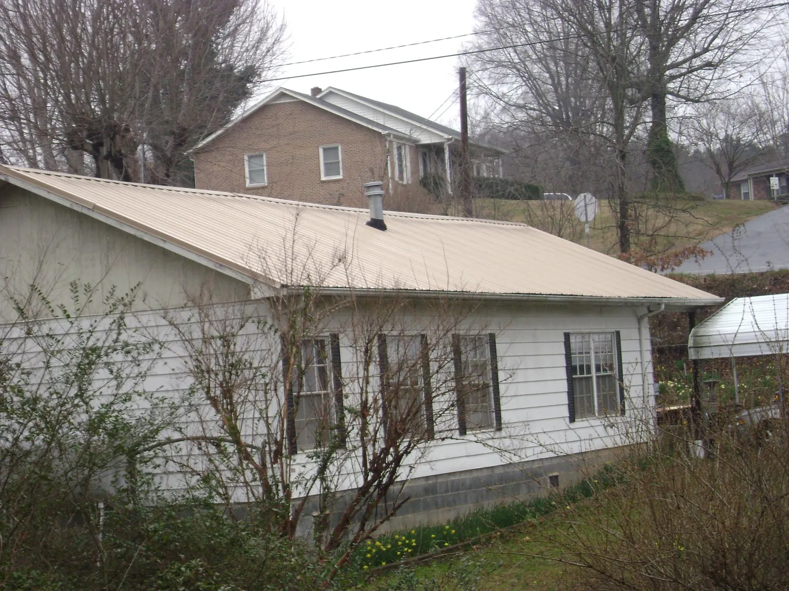 Tan metal roof on a white sided house set into a hillside — Commercial Roofing by Roofing Brothers in Forest Lake